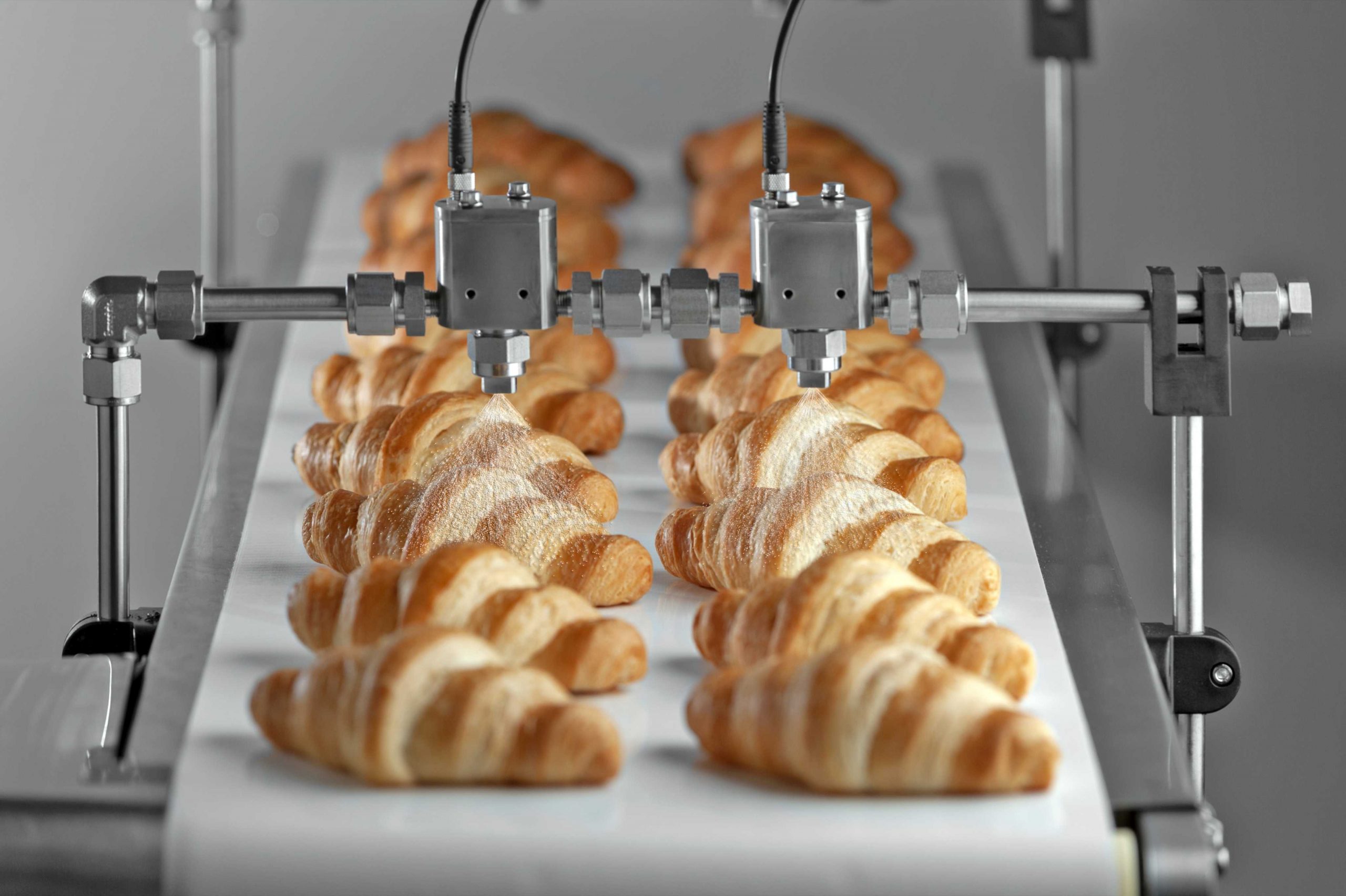 BETE FlexFlow Precision Spray Control System with Electric HydroPulse Automatic Spray Nozzles Spraying Croissants on a Bakery Conveyor Coating Application