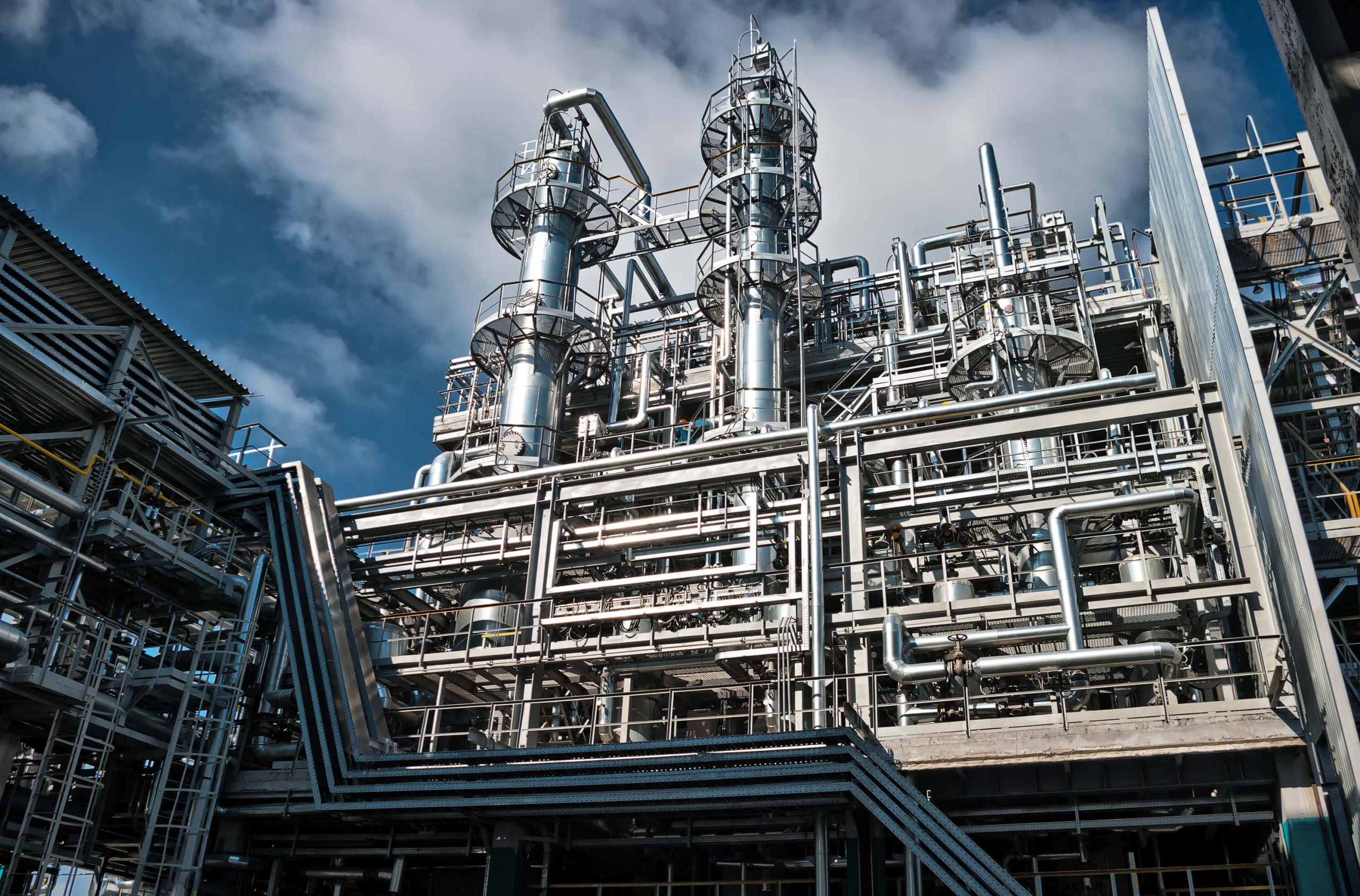 Looking up at a chemical processing plant with towers, ducts, and pipes where chemical injection application processing occurs.